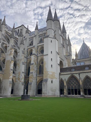 Gothic-style cathedral with tall spires and arched windows, adjacent to a green lawn and a small statue in the foreground.
