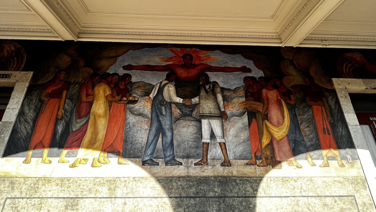Mural depicting two men shaking hands in the center, surrounded by people on both sides, with a large red figure in the background.