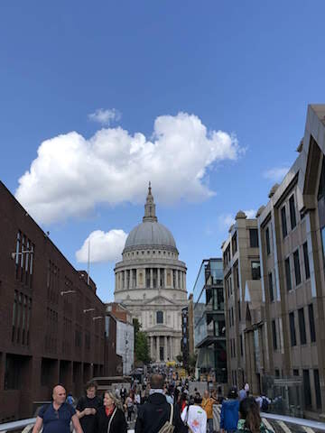 People walk on a city street with St. Pauls Cathedral in the background under a partly cloudy sky.