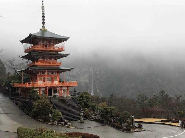 An orange and black temple in a misty forest in Japan.
