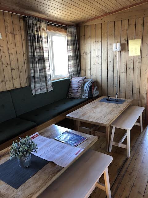 Wood-paneled room with a window, green cushioned bench, wooden tables, benches, potted plant, and papers on the table.