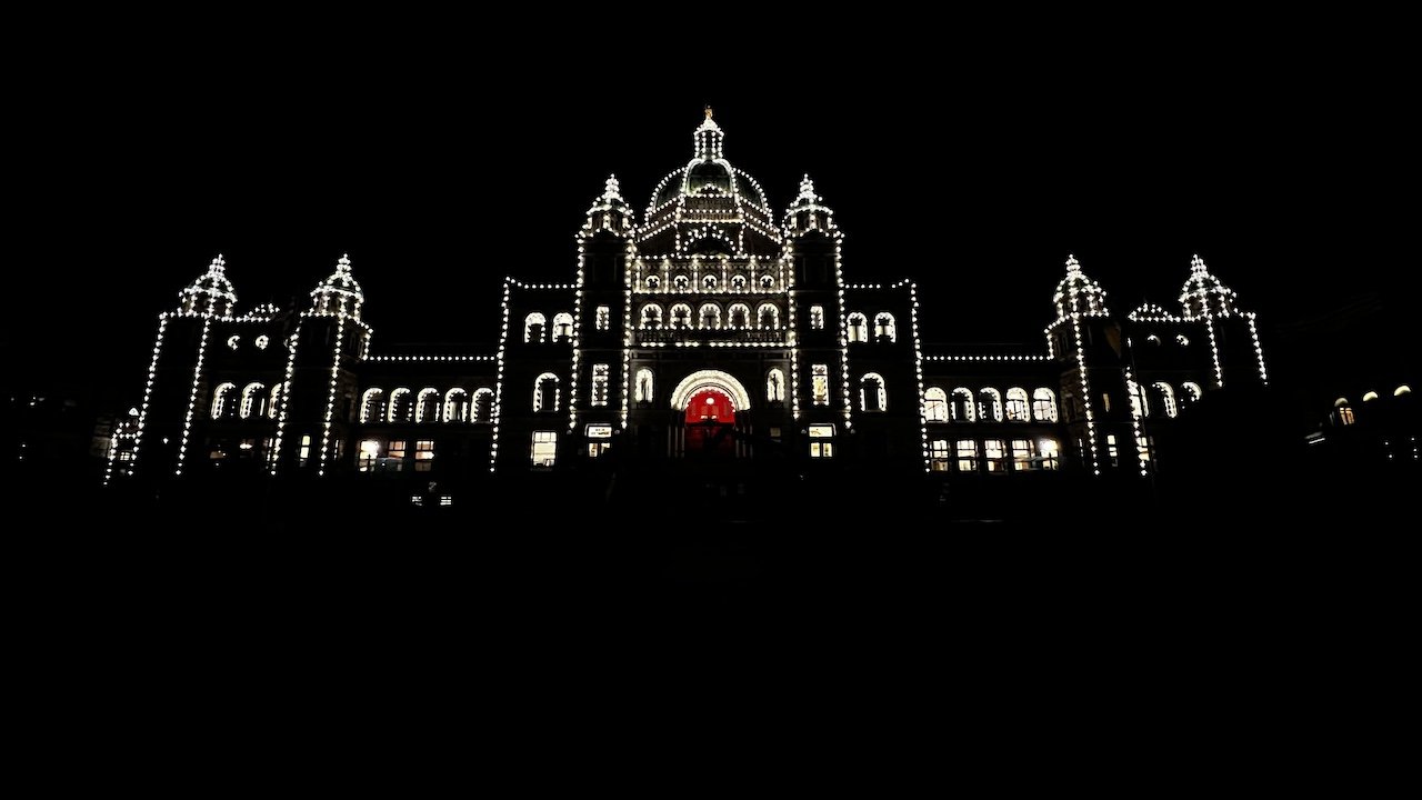 A large domed building in Victoria, British Columbia, outlined with white lights, stands illuminated against a black night sky.