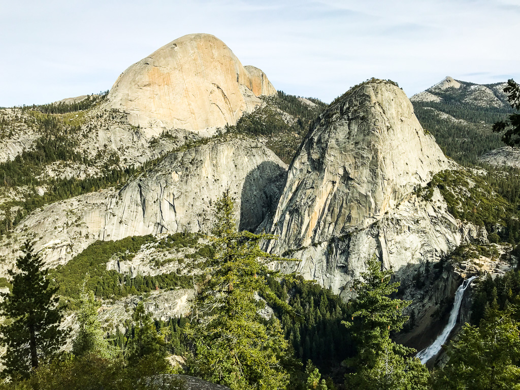 Granite domes and cliffs with pine trees and a waterfall in Yosemite National Park under a clear sky.