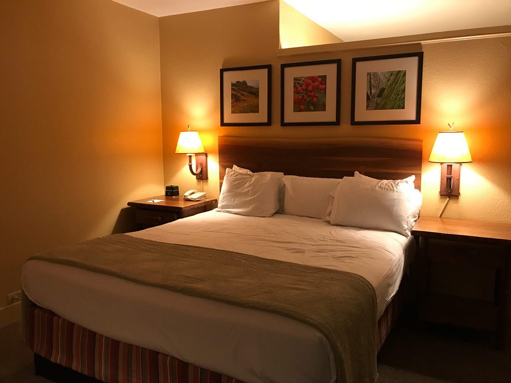 A hotel room with a neatly made king bed, two nightstands with lamps, and three framed pictures above the headboard.