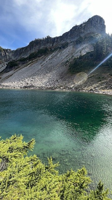 Clear lake with green water bordered by rocky cliffs and sparse vegetation under a partly cloudy sky.