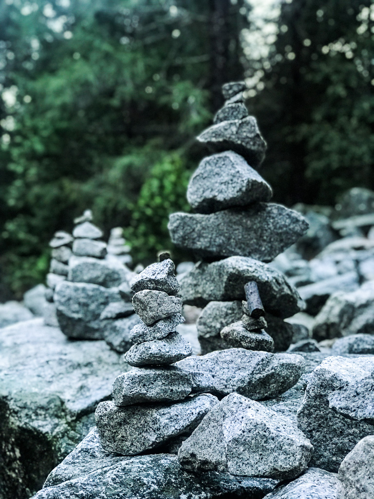 Several stacks of balanced stones are arranged outdoors on a rocky surface with trees in the background.