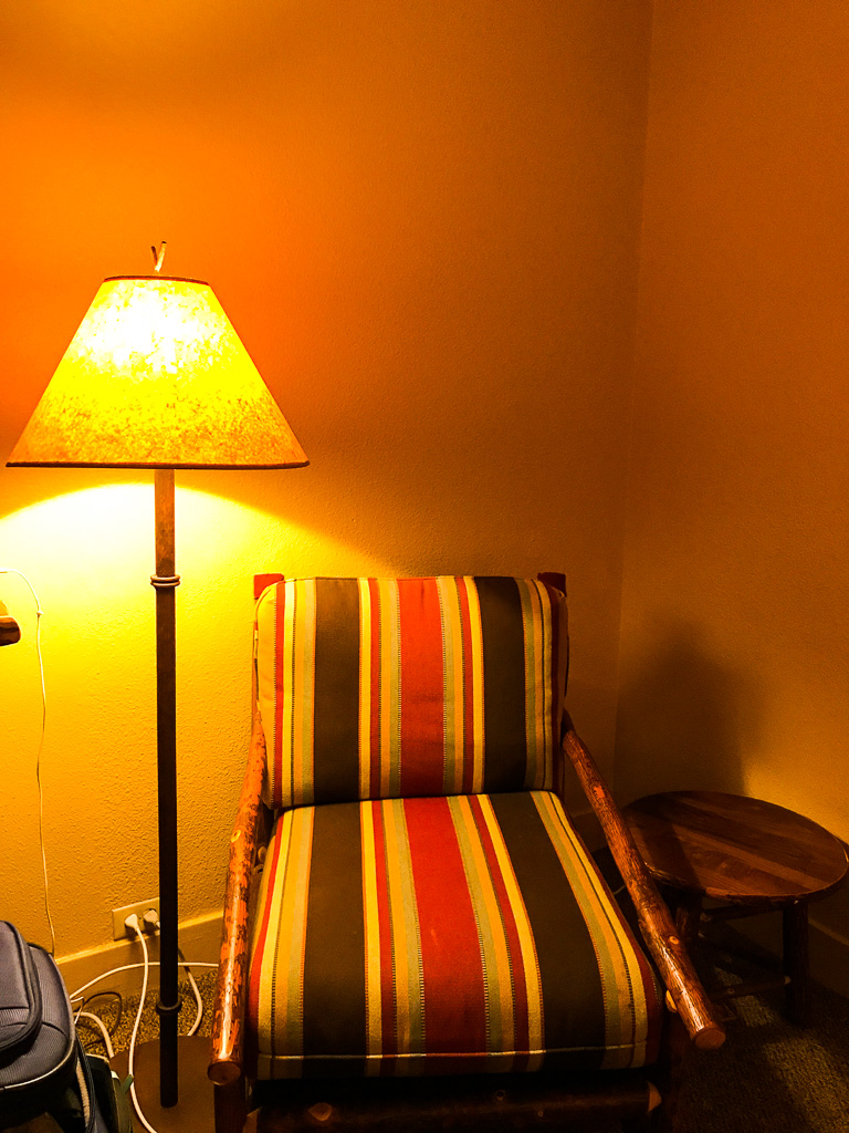 A striped armchair next to a floor lamp and a small round wooden table in the corner of a warmly lit room.