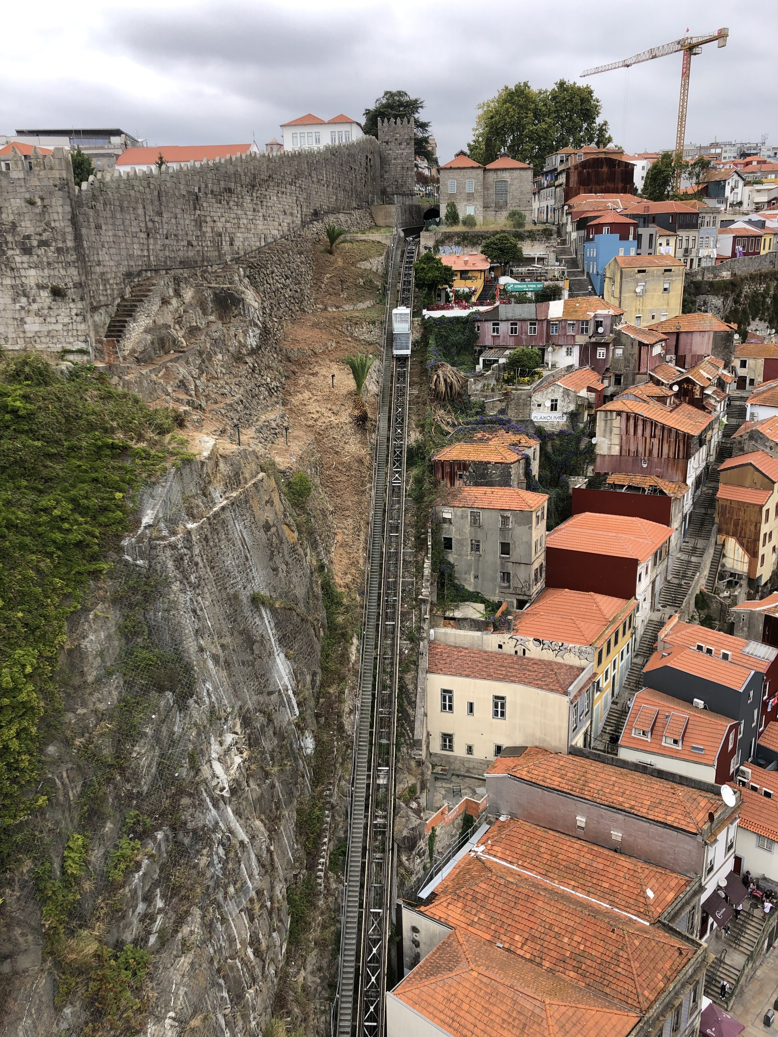 A funicular railway ascends a steep hillside beside stone walls and colorful buildings in an urban area.