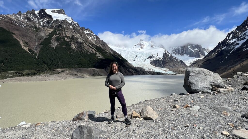 Person stands on rocky ground by a milky lake, glacier, and snow-capped peaksโan iconic stop on any Patagonia itinerary.