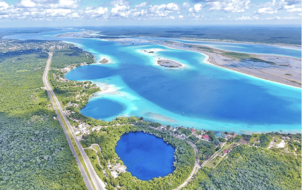 Aerial view of a lagoon near Tulum with turquoise waters, green land, roads, and buildings—perfect for your next Tulum Travel Guide adventure.
