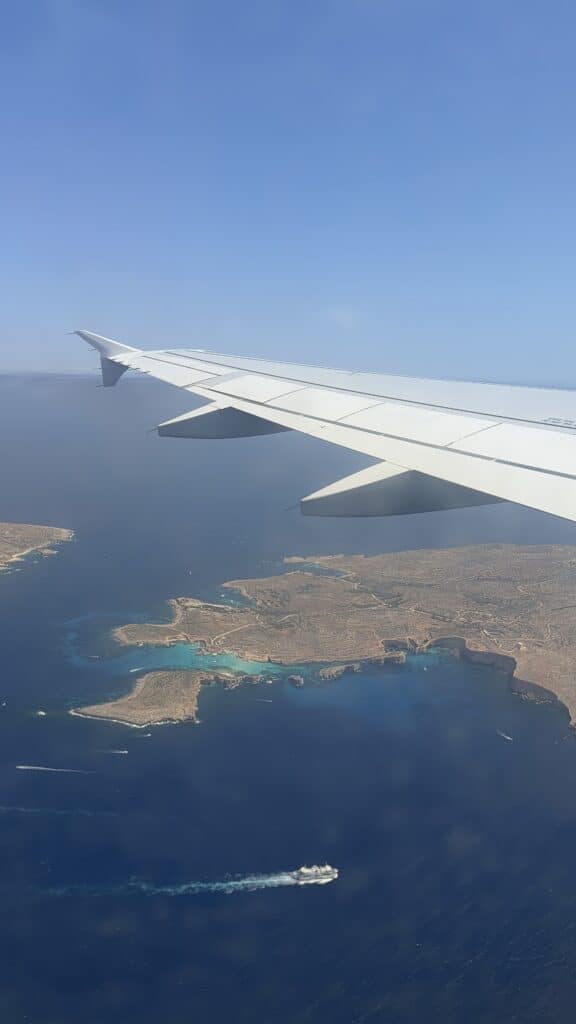 View from airplane window: wing over Malta’s blue coast, islands, and a boat—perfect start to your Malta itinerary or 3 day Malta adventure.