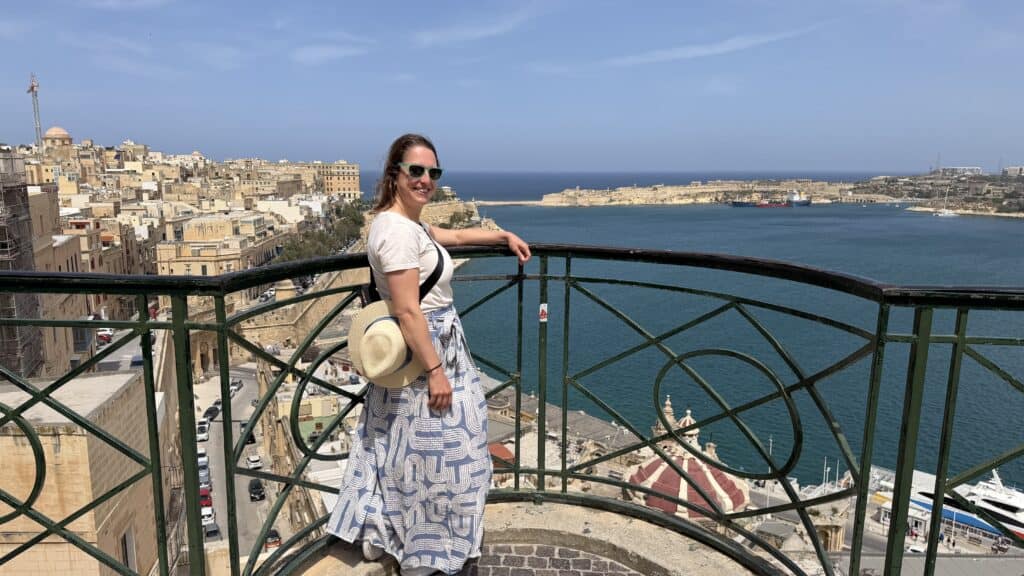 Woman in sunglasses and a white skirt stands on a balcony overlooking Malta’s coast—perfect inspiration for a 3 day Malta itinerary.