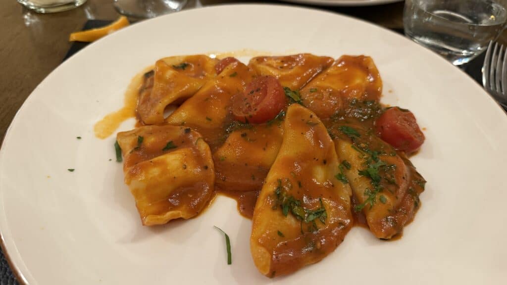 Plate of ravioli with tomato sauce and herbs, perfect after exploring your Malta itinerary; served on a white dish with a fork and glass nearby.