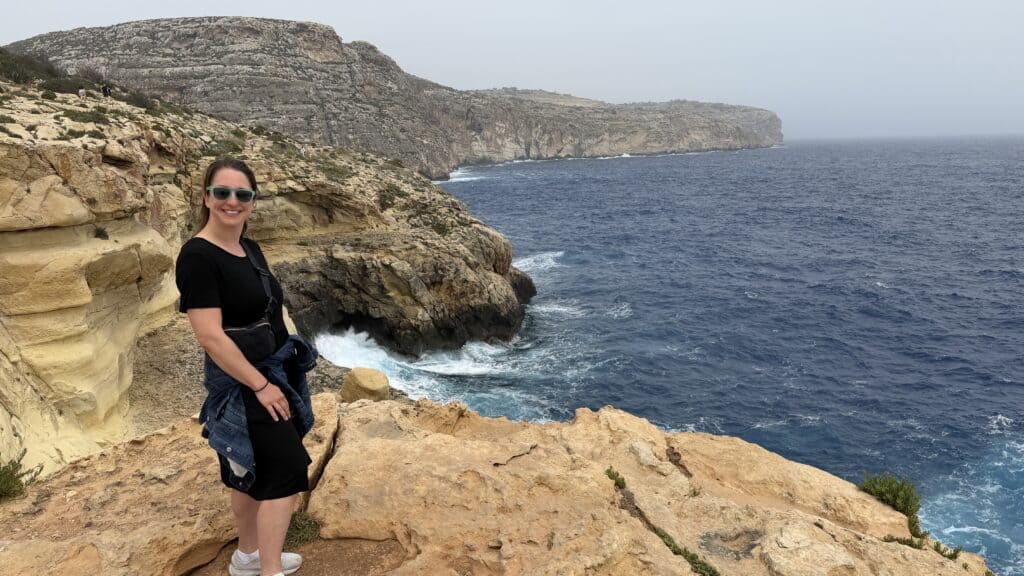 Person in sunglasses stands on a rocky cliff, enjoying ocean views—perfect moment for any Malta Itinerary or 3 Day Malta Itinerary.