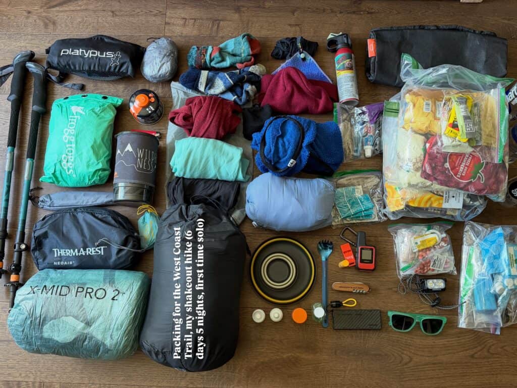 Backpacking gear for hiking the Pacific Crest Trail laid out: tent, sleeping bag, food, clothes, cookware, water bottle, trekking poles.