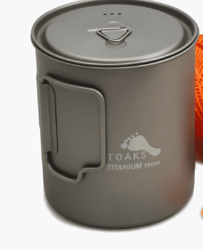 A grey titanium camping mug with lid and foldable handle, ideal backpacking gear for the Pacific Crest Trail. Orange mesh bag partially visible.