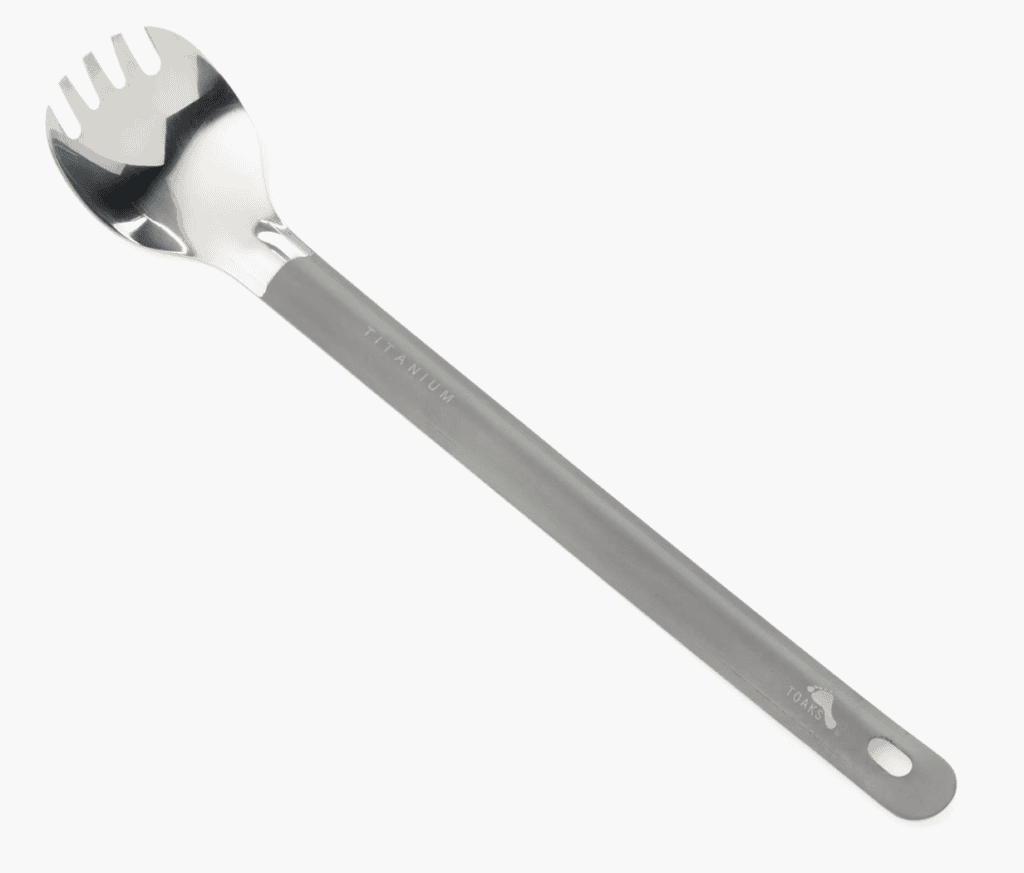 A long-handled, silver titanium spork—essential hiking equipment for the Pacific Crest Trail—with a slotted spoon end and handle hole.