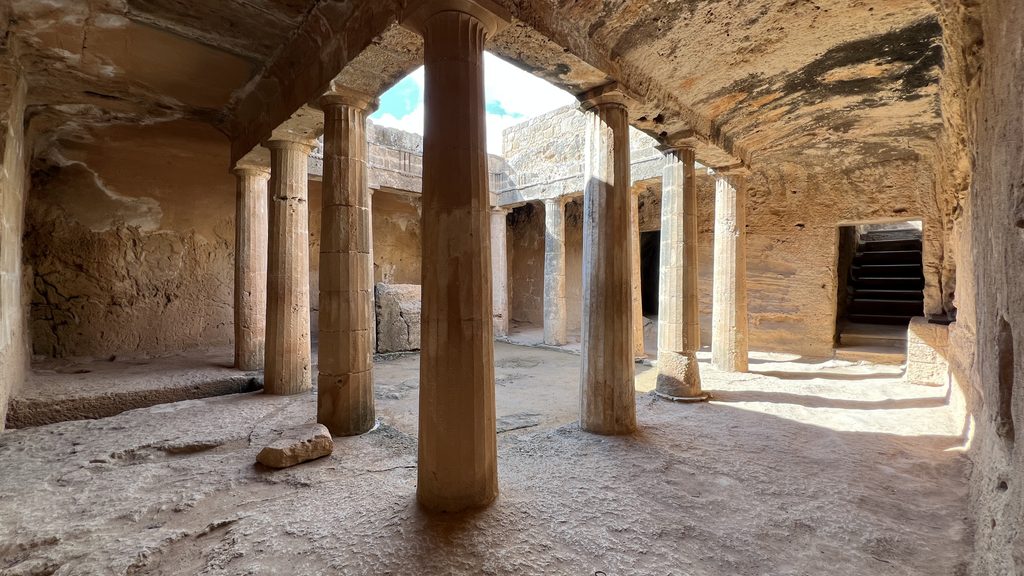 An open-air courtyard with stone columns and carved rock walls at the Tombs of the Kings, a must-see for your Cyprus itinerary.