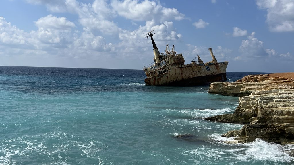 A rusted shipwreck listing in the sea off a rocky coastline, a highlight of a Cyprus travel guide.