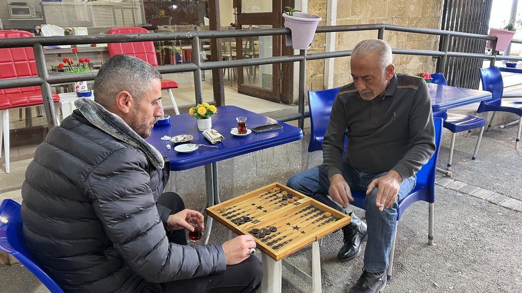 Two men sitting at an outdoor table playing backgammon while visiting Cyprus.